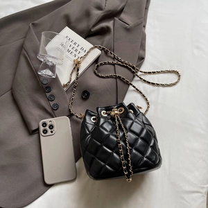 Detail of black quilted bucket bag with gold chain strap on minimalist lifestyle background