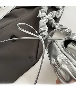 Detail of silver pleated cloud bag featuring delicate leather bow and metallic finish texture