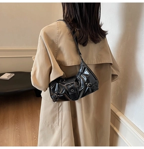 Close-up of black glossy leather underarm bag with large buckle on beige trench coat