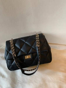 Detail shot of black quilted faux leather handbag with golden chain and metal turn lock