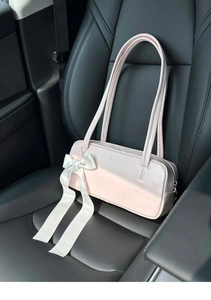Pink bow shoulder bag on a black leather seat showing smooth texture and chic design