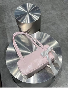 Detail of pink faux leather shoulder bag featuring a white satin bow on a metal stand