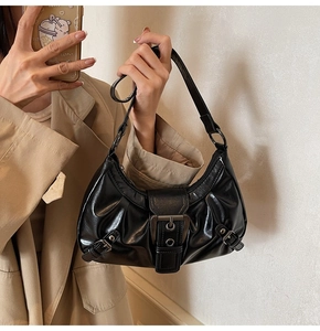 Detail of black glossy shoulder bag featuring retro silver buckles and pleated leather texture