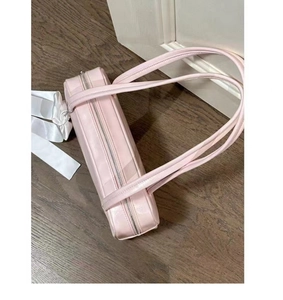 Detailed side view of pink bow baguette bag with silver zipper on wooden floor
