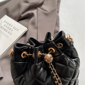 Detail shot of black quilted bucket bag featuring gold-tone chain and branded metal sphere