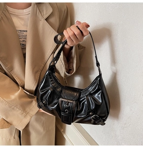 Close-up of ruched black crescent bag with polished metal buckle and shiny finish