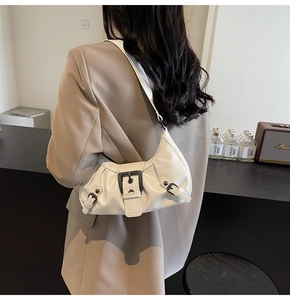 Detail of white patent leather crescent bag with metallic buckle on a model's shoulder