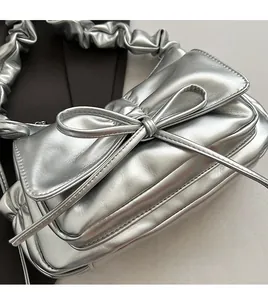 Detail of silver metallic cloud bag featuring large bow and pleated scrunchie handle