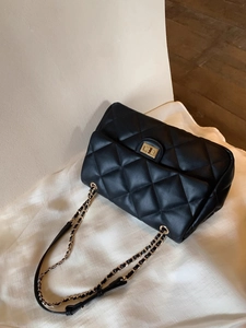 Close-up of black quilted leather texture and gold-tone metal chain on crossbody bag