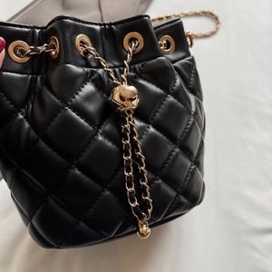 Close-up of black quilted bucket bag featuring drawstring and gold chain strap
