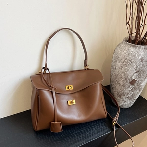 Sac fourre-tout en cuir marron avec fermoir doré et bandoulière sur socle minimal