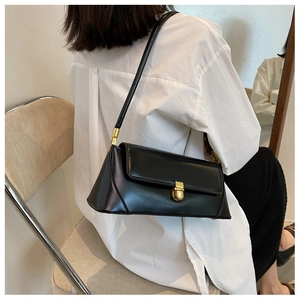 Detail of a black glossy leather underarm bag with an elegant gold metal clasp on a model