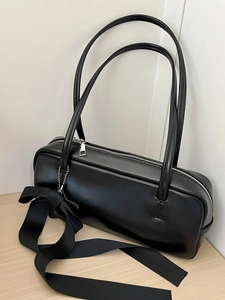 Detail of a black underarm bag featuring a smooth texture and a large silk bow decoration
