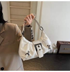 Detail of white glossy crescent bag with vintage metal buckles and punk rivet accents