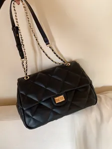 Detailed macro view of quilted leather texture and golden metal chain strap on black bag