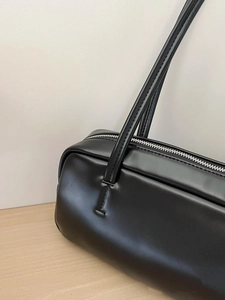 Detail view of the sleek black cylinder bag with long shoulder strap and silver zipper
