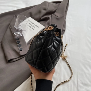 Detailed view of black quilted bucket bag with gold chain strap on grey blazer