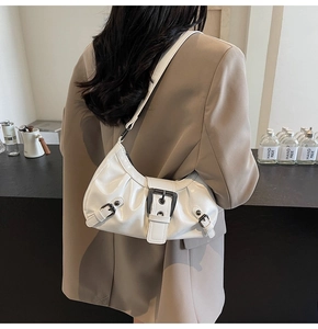 Detail of white pleated shoulder bag with black metal buckles on a blazer model