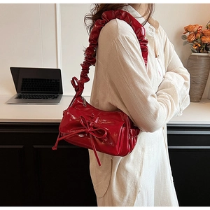 Detail of red glossy patent leather pleated shoulder bag with decorative bow and cloud strap