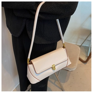 Detail of a creamy white underarm bag with brown trim and a gold rectangular metal clasp