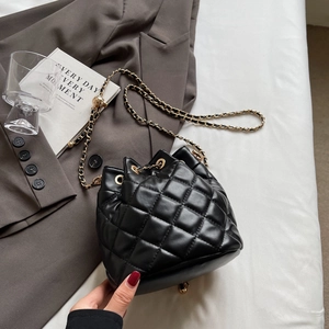 Close-up of black quilted bucket bag with gold chain strap on a minimalist background