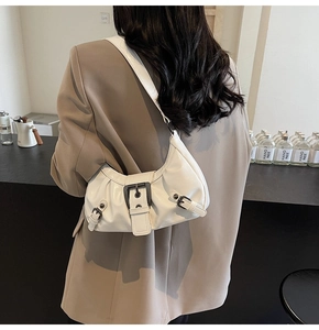 Detail of creamy white glossy shoulder bag showing soft pleats and dark metal buckle