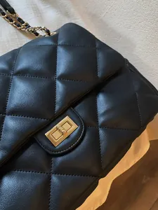 Macro detail of quilted black leather texture and golden square metal twist lock on bag