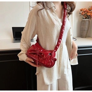 Close-up of shiny red patent leather shoulder bag with bow detail and pleated strap