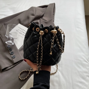 Detail of black quilted bucket bag with gold chain strap and drawstring closure