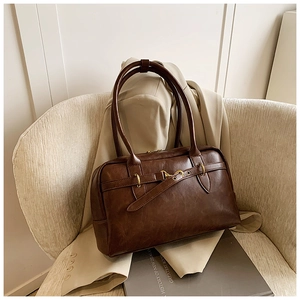 Détail du sac cabas en similicuir marron foncé avec boucles dorées sur un canapé chic