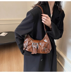 Close-up of vintage brown underarm bag featuring glossy pleated leather and wide buckle strap