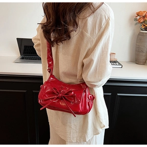 Detail of red glossy patent leather shoulder bag with matching bow on a female model