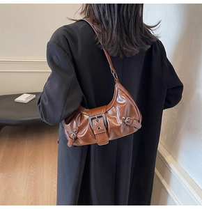 Brown half-moon shoulder bag in glossy leather texture worn by a model in a warm room