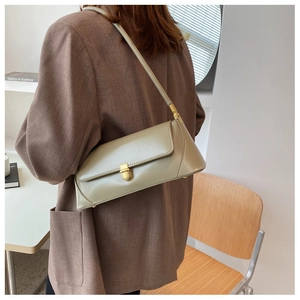 Detail of sage green rectangular underarm bag with gold lock on a model in a brown blazer