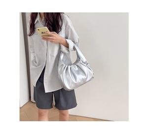 Silver metallic pleated cloud bag worn by a model in a stylish indoor setting
