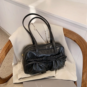 Detail of black faux leather tote with decorative bows and pleated pockets on a beige blazer