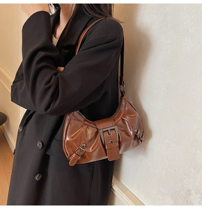 Brown leather shoulder bag shown on model with vintage buckles and glossy finish