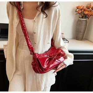Detail of red patent leather shoulder bag with a large bow and pleated scrunchie strap