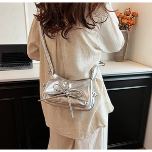 Detail of silver metallic pleated bag with bow, shown worn by a model in a modern room