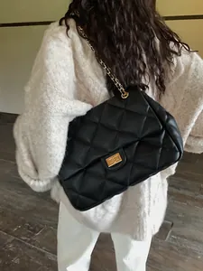 Detailed view of black quilted chain bag with gold hardware worn on model's shoulder