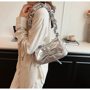 Close-up of metallic silver underarm bag featuring a bow and pleated shoulder strap