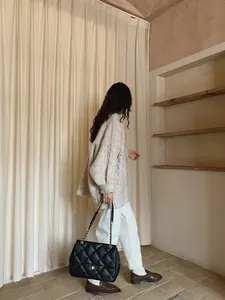 Detailed view of black quilted chain bag paired with a beige knit cardigan and white trousers