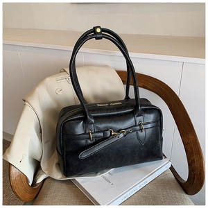 Vue détaillée du sac Boston noir avec boucle dorée sur chaise en bois et livre