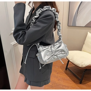 Close-up of metallic silver cloud bag featuring bow detail and pleated shoulder strap