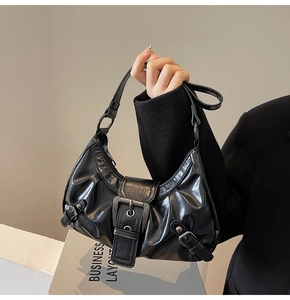 Close-up of black glossy shoulder bag featuring soft pleats and bold silver buckle detail