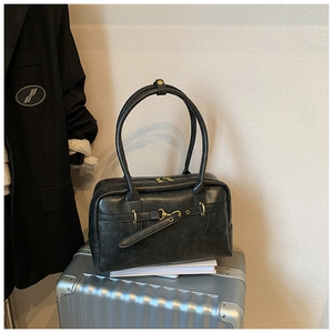 Détail d'un sac Boston en cuir noir avec boucle dorée sur une valise argentée