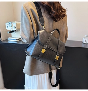 Close-up of a vintage black leather messenger bag with gold buckles in a coffee shop setting