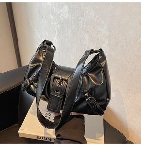 Detail of black faux leather shoulder bag with vintage metal buckle and pleated design