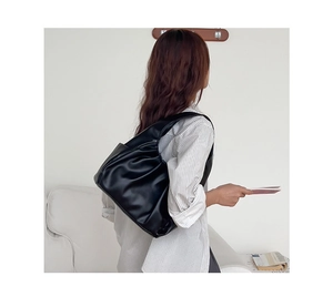 Detail of black pleated croissant bag with soft leather texture shown on shoulder