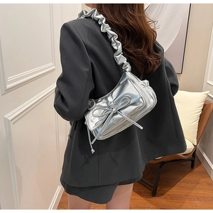 Detail of silver metallic cloud bag featuring large bow and pleated shoulder strap design